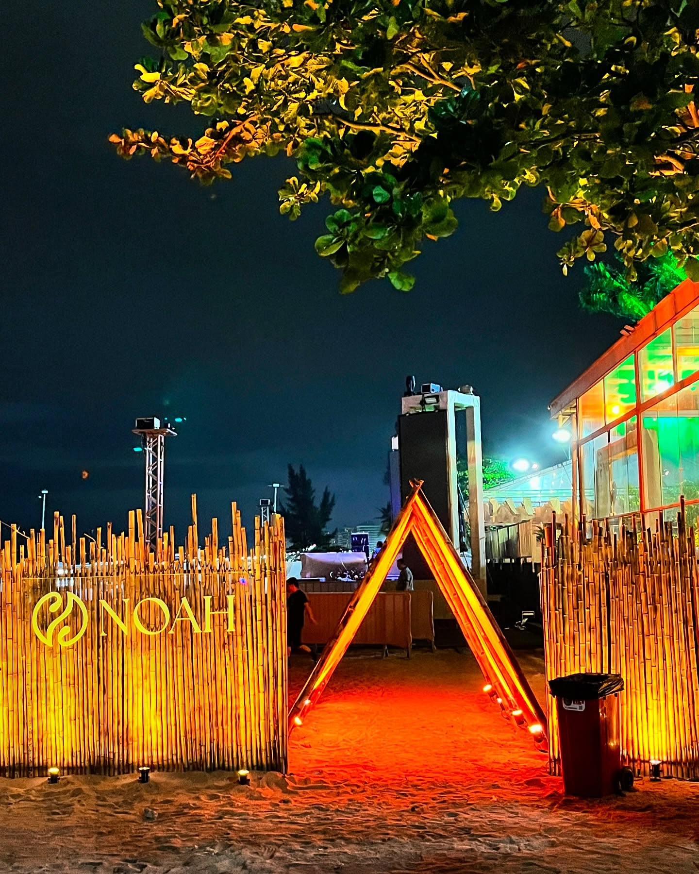 Entrada cenográfica NOAH - bambu iluminado e portal triangular na praia